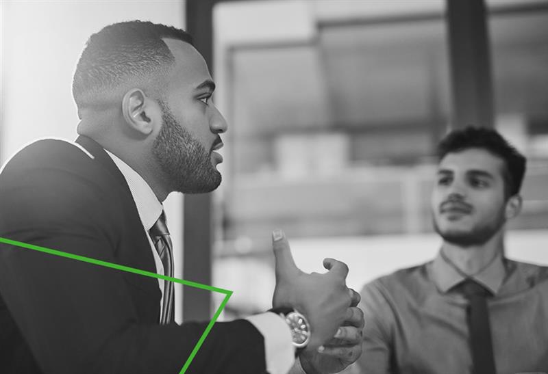 Deux collègues masculins dans un bureau, engagés dans une réunion d'affaires. L’un parle et l’autre écoute attentivement.