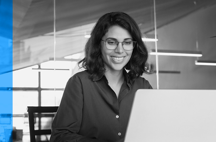 Une femme avec des lunettes, souriante et travaillant sur un ordinateur portable.