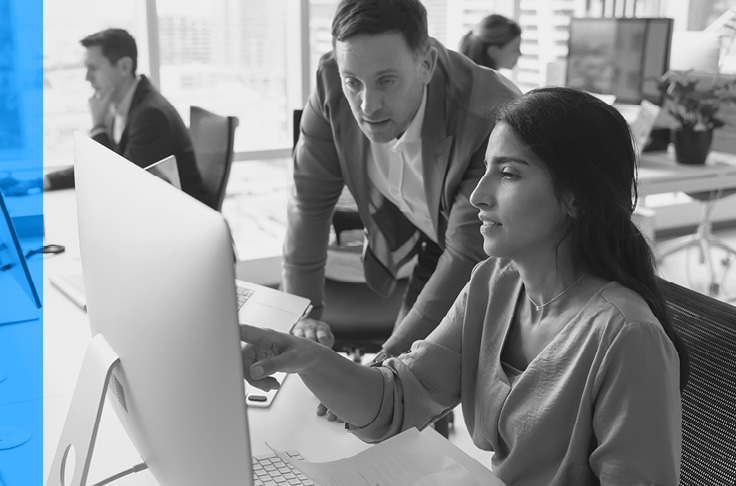 Deux collègues, un homme et une femme, examinent leur travail sur un ordinateur dans un bureau.
