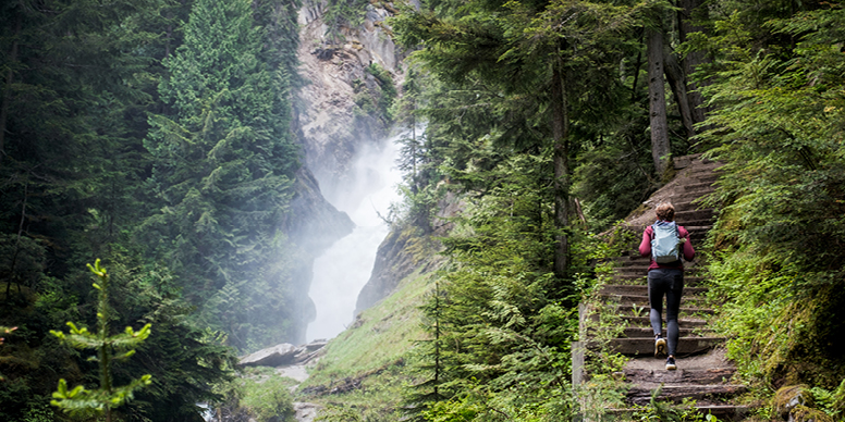 Randonneuse montant les escaliers dans une forêt tout en admirant une cascade.