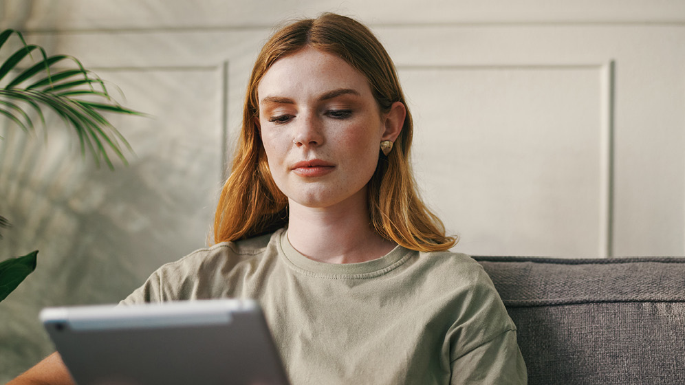 A woman sitting on the couch studies her tablet screen. 