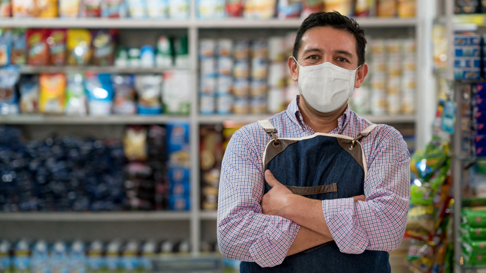 Employé d’une épicerie portant un masque de protection devant des étagères remplies de nourriture 